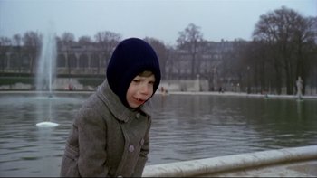 Movie still from “The Tenant” (1976), directed by Roman Polanski – A little boy wearing a coat and a hat by the water; Medium shot, Low angle
