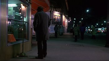 Movie still from “The Tenant” (1976), directed by Roman Polanski – A man standing on the sidewalk in the dark; Wide shot, Over the shoulder angle