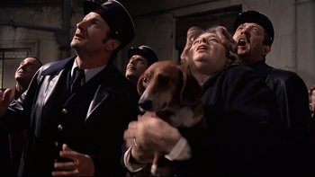 Movie still from “The Tenant” (1976), directed by Roman Polanski – A group of men and a woman holding a brown dog; Medium shot, Low angle