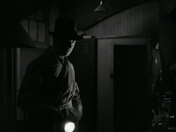 Movie still from “The Thin Man” (1934), directed by W.S. Van Dyke – A man standing in a dark room holding a flashlight; Medium shot, Low angle