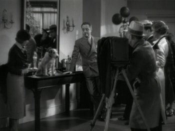Movie still from “The Thin Man” (1934), directed by W.S. Van Dyke – A man in a suit and tie standing in front of a camera; Wide shot, High angle