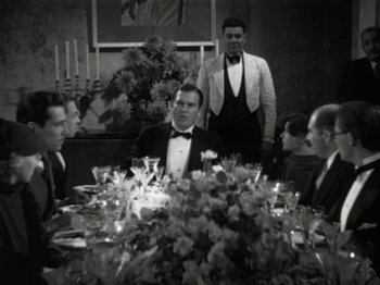 Movie still from “The Thin Man” (1934), directed by W.S. Van Dyke – A group of men sitting at a table with a flower arrangement; Medium shot, Low angle