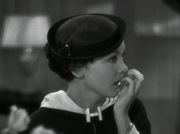 Movie still from “The Thin Man” (1934), directed by W.S. Van Dyke – A woman wearing a hat is holding her hand to her mouth; Close Up shot, Over the shoulder angle