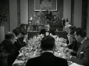 Movie still from “The Thin Man” (1934), directed by W.S. Van Dyke – A group of people sitting around a table with wine glasses on it; Wide shot, High angle