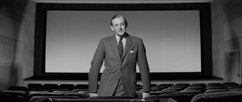Movie still from “The Three Faces of Eve” (1957), directed by Nunnally Johnson – An older man standing in front of a projector screen; Medium shot, Low angle