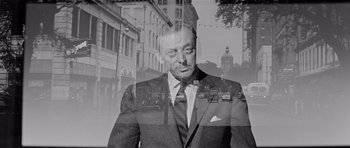 Movie still from “The Three Faces of Eve” (1957), directed by Nunnally Johnson – A man in a suit and tie standing in front of a building; Close Up shot, Low angle