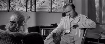 Movie still from “The Three Faces of Eve” (1957), directed by Nunnally Johnson – A black and white photo of a man handing a paper to another man; Medium shot, Over the shoulder angle