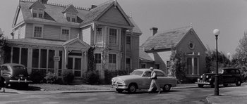Movie still from “The Three Faces of Eve” (1957), directed by Nunnally Johnson – A man walking down the street past a car; Wide shot, Low angle