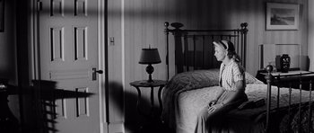Movie still from “The Three Faces of Eve” (1957), directed by Nunnally Johnson – A woman sitting on a bed next to a nightstand; Wide shot, High angle