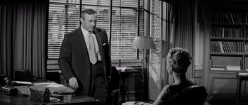Movie still from “The Three Faces of Eve” (1957), directed by Nunnally Johnson – A man in a suit standing next to a woman in front of a window; Medium shot, Over the shoulder angle