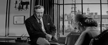 Movie still from “The Three Faces of Eve” (1957), directed by Nunnally Johnson – An older man in a suit and tie sitting next to a woman in front of a window; Medium shot, Over the shoulder angle
