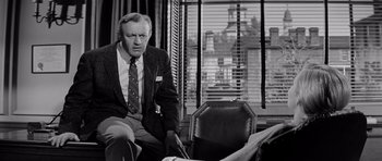 Movie still from “The Three Faces of Eve” (1957), directed by Nunnally Johnson – An older man sitting in a chair in front of a window; Medium shot, Low angle