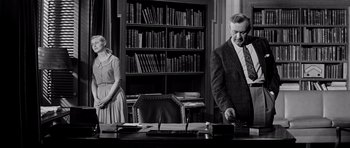 Movie still from “The Three Faces of Eve” (1957), directed by Nunnally Johnson – An old photo of a man and a woman standing at a desk in front of a book case; Medium shot, Low angle