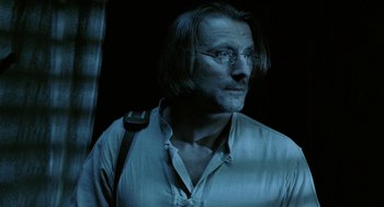 Movie still from “The Ugly Swans” (2006), directed by Konstantin Lopushanskiy – A man with long hair wearing glasses and a white shirt; Close Up shot, Low angle