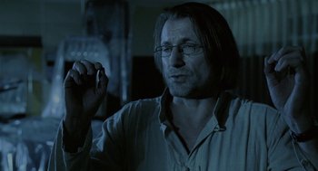 Movie still from “The Ugly Swans” (2006), directed by Konstantin Lopushanskiy – A man with glasses is holding something in his hand; Close Up shot, Over the shoulder angle