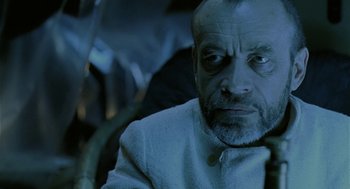 Movie still from “The Ugly Swans” (2006), directed by Konstantin Lopushanskiy – An older man with a goatee looking at the camera; Close Up shot, Over the shoulder angle
