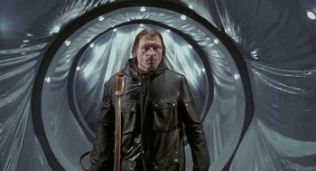 Movie still from “The Ugly Swans” (2006), directed by Konstantin Lopushanskiy – A man wearing a black jacket and a brown bag; Medium shot, Low angle