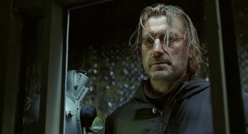 Movie still from “The Ugly Swans” (2006), directed by Konstantin Lopushanskiy – A person wearing glasses and a jacket; Close Up shot, Low angle