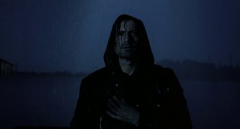 Movie still from “The Ugly Swans” (2006), directed by Konstantin Lopushanskiy – A man in a hooded jacket standing in the dark; Medium shot, Low angle