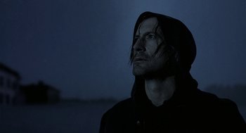 Movie still from “The Ugly Swans” (2006), directed by Konstantin Lopushanskiy – A man in a hooded jacket looking up into the sky; Close Up shot, Low angle