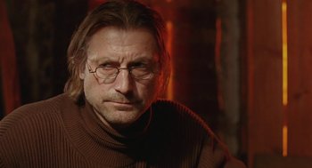 Movie still from “The Ugly Swans” (2006), directed by Konstantin Lopushanskiy – A person wearing glasses and a sweater; Close Up shot, Over the shoulder angle