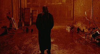 Movie still from “The Ugly Swans” (2006), directed by Konstantin Lopushanskiy – A man in a long black coat standing in the rain; Wide shot, Low angle