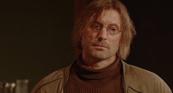 Movie still from “The Ugly Swans” (2006), directed by Konstantin Lopushanskiy – A person wearing glasses and a jacket; Close Up shot, Over the shoulder angle