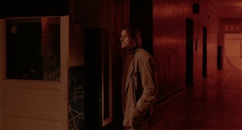 Movie still from “The Ugly Swans” (2006), directed by Konstantin Lopushanskiy – A man standing next to a door in a dark room; Wide shot, Over the shoulder angle