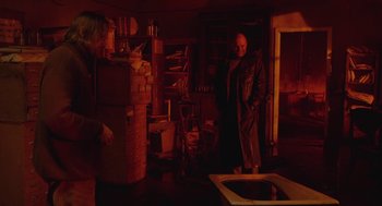 Movie still from “The Ugly Swans” (2006), directed by Konstantin Lopushanskiy – A man standing in a room with boxes on the floor; Wide shot, Over the shoulder angle