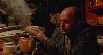 Movie still from “The Ugly Swans” (2006), directed by Konstantin Lopushanskiy – A man sitting at a table clapping his hands; Medium shot, Low angle