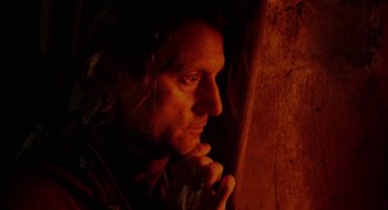 Movie still from “The Ugly Swans” (2006), directed by Konstantin Lopushanskiy – A man with long black hair is looking out a window; Close Up shot, Low angle