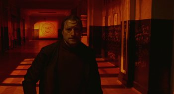 Movie still from “The Ugly Swans” (2006), directed by Konstantin Lopushanskiy – A man in a black jacket standing next to a wall; Medium shot, Low angle