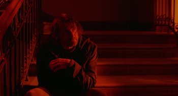 Movie still from “The Ugly Swans” (2006), directed by Konstantin Lopushanskiy – A man sitting on the steps in a dark room; Medium shot, Low angle