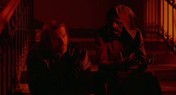 Movie still from “The Ugly Swans” (2006), directed by Konstantin Lopushanskiy – Two people sitting in a dark room , one of them wearing a mask; Medium shot, Over the shoulder angle
