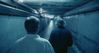 Movie still from “The Ugly Swans” (2006), directed by Konstantin Lopushanskiy – Two men are walking down a long hallway; Wide shot, High angle