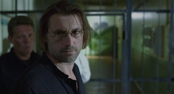 Movie still from “The Ugly Swans” (2006), directed by Konstantin Lopushanskiy – A person wearing glasses in a room; Close Up shot, Over the shoulder angle