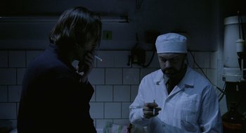 Movie still from “The Ugly Swans” (2006), directed by Konstantin Lopushanskiy – A man smoking a cigarette next to another man in a white lab coat; Medium shot, Low angle
