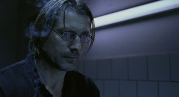 Movie still from “The Ugly Swans” (2006), directed by Konstantin Lopushanskiy – A person wearing glasses and a black shirt; Close Up shot, Over the shoulder angle
