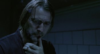 Movie still from “The Ugly Swans” (2006), directed by Konstantin Lopushanskiy – A man with a beard and glasses in a dark room; Close Up shot, Low angle