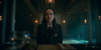 Movie still from “The Umbrella Academy” (2019), created by Steve Blackman – A woman is sitting at a table in front of a window; Close Up shot, Low angle
