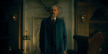 Movie still from “The Umbrella Academy” (2019), created by Steve Blackman – An older man in a suit and tie in front of a fireplace; Medium shot, Low angle