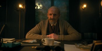 Movie still from “The Umbrella Academy” (2019), created by Steve Blackman – An older man sitting at a table with a cup of coffee; Medium shot, Low angle
