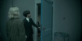 Movie still from “The Umbrella Academy” (2019), created by Steve Blackman – A man in a suit opens a blue door; Medium shot, Over the shoulder angle