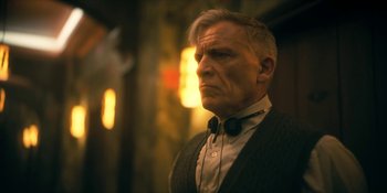 Movie still from “The Umbrella Academy” (2019), created by Steve Blackman – An older man wearing a suit and bow tie looking to his left; Close Up shot, Low angle