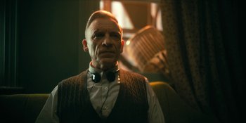 Movie still from “The Umbrella Academy” (2019), created by Steve Blackman – An older man wearing a bow tie in a room; Close Up shot, Low angle