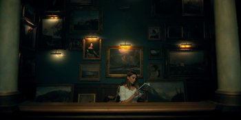 Movie still from “The Umbrella Academy” (2019), created by Steve Blackman – A woman sitting at a table reading a book; Wide shot, Low angle