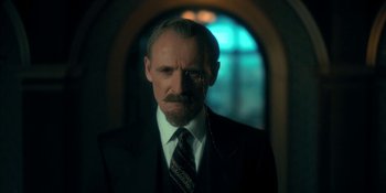 Movie still from “The Umbrella Academy” (2019), created by Steve Blackman – A man with a beard and mustache wearing a suit and tie; Close Up shot, Low angle