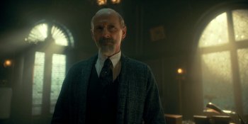 Movie still from “The Umbrella Academy” (2019), created by Steve Blackman – An older man in a suit and tie in a dark room; Medium shot, Low angle