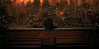 Movie still from “The Umbrella Academy” (2019), created by Steve Blackman – A man sitting on top of a bench in front of a city; Wide shot, High angle