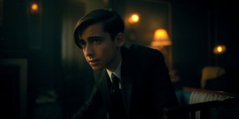 Movie still from “The Umbrella Academy” (2019), created by Steve Blackman – A man in a suit and tie sitting in a room; Close Up shot, Low angle